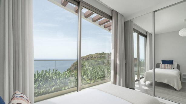 Ein Schlafzimmer mit großem Fenster und Blick auf das Meer und die grüne Umgebung.