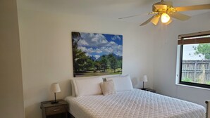 A bedroom with a bed, two bedside tables, a ceiling fan, a window with a view of greenery, and a painting on the wall. - Cozy family home in quiet area, nice garden views. (Miami)