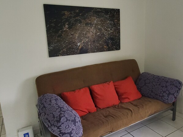 En brun sofa med puder i rødt og lilla med blomstermønster, et sort abstrakt maleri på væggen og en hvid genstand på gulvet.