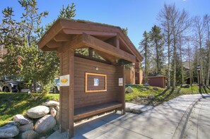 A wooden cabin with a bench in front, surrounded by trees and rocks.