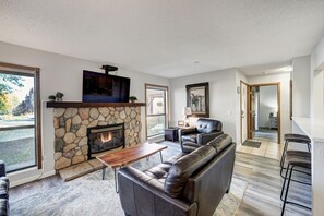 A modern living room with a stone fireplace, leather sofa, and a television mounted above it. - Base 9 B101 (Breckenridge)