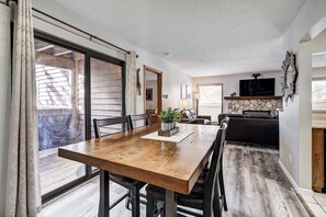 A dining area with a wooden table and chairs, a potted plant, and a view through a sliding glass door to the outside.