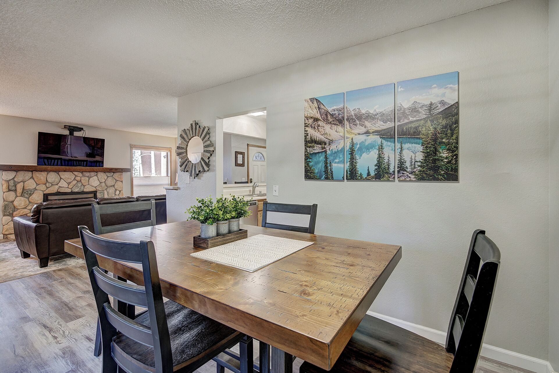 A dining area with a wooden table, chairs, and a stone fireplace. There is a painting of a mountain landscape on the wall.