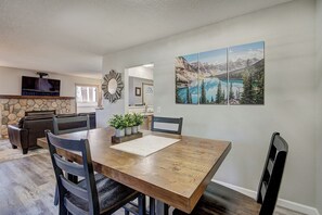 A dining area with a wooden table, chairs, and a stone fireplace. There is a painting of a mountain landscape on the wall. - Base 9 B101 (Breckenridge)
