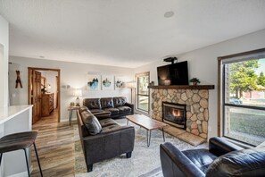 A modern living room with a stone fireplace, leather sofas, and a large window offering a view of the outdoors.
