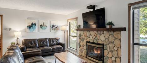 A living room with a stone fireplace, leather sofas, a coffee table, and artwork on the wall.