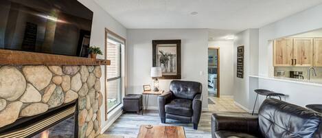 A living room with a stone fireplace, leather furniture, and a kitchen area in the background.