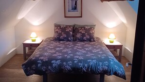 Une chambre à coucher avec un lit, deux tables de chevet avec des lampes, un tableau encadré au mur et un plafond en pente.