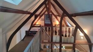 Une chambre à coucher aménagée dans un grenier, avec un plafond en pente, des poutres en bois, un lit superposé, un bureau et un escalier.