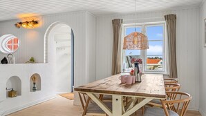 Un coin repas avec une table et des chaises en bois, un luminaire suspendu et une vue par la fenêtre.