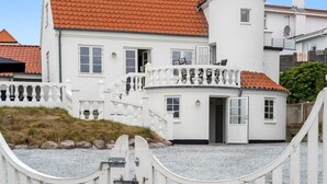 Un bâtiment blanc surmonté d’un toit recouvert de tuiles rouges, doté d’un balcon avec des balustrades blanches et d’une petite structure en forme de tourelle.