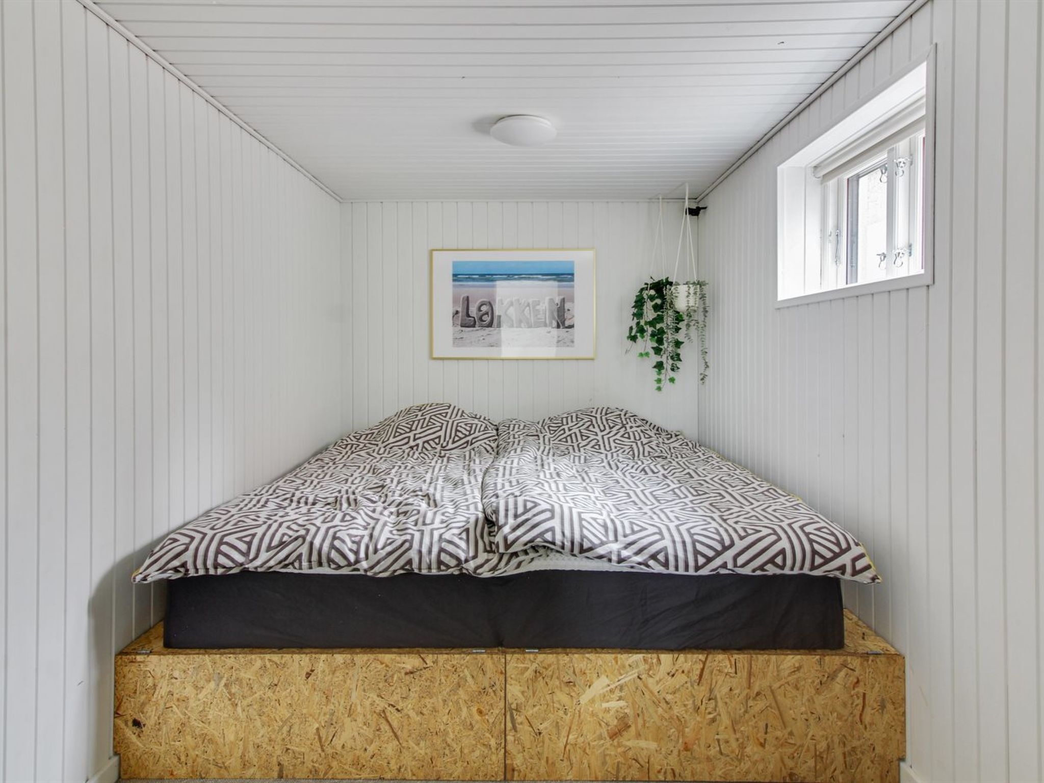 A bedroom with a bed, a framed picture on the wall, and a window.