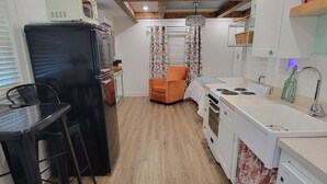 A compact kitchen with a black refrigerator, a dining table with chairs, a wooden floor, and a chandelier.