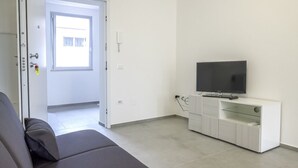 A modern living room with a sofa, a television on a white cabinet, and a door leading to another room. - SE029 - Mondolfo, new three-room apartment with balcony and air conditioning (Mondolfo)