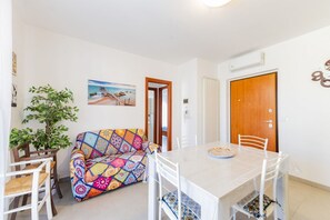 A dining area with a table, chairs, a colorful sofa, a potted plant, and a painting on the wall.