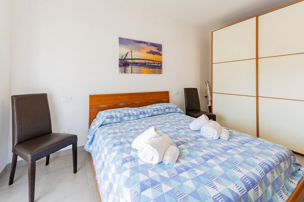 A hotel room with a bed, a chair, a painting of a bridge, and a large wardrobe.