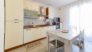 Una cuina moderna amb armaris blancs, microones, fogó i zona de dinar amb taula i cadires.