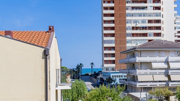 Un edifici de diverses plantes amb balcons, vista clara al mar i una zona d'aparcament al primer terme.