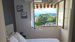 Une chambre à coucher avec un lit, une fenêtre donnant sur la ville et deux tableaux représentant des fleurs, accrochés au mur.