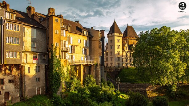Un bâtiment historique à étages, doté d’une tour imposante et entouré d’un jardin.