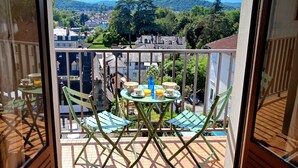 Un balcon avec une table dressée pour deux personnes, des chaises et une vue sur la ville et les montagnes.
