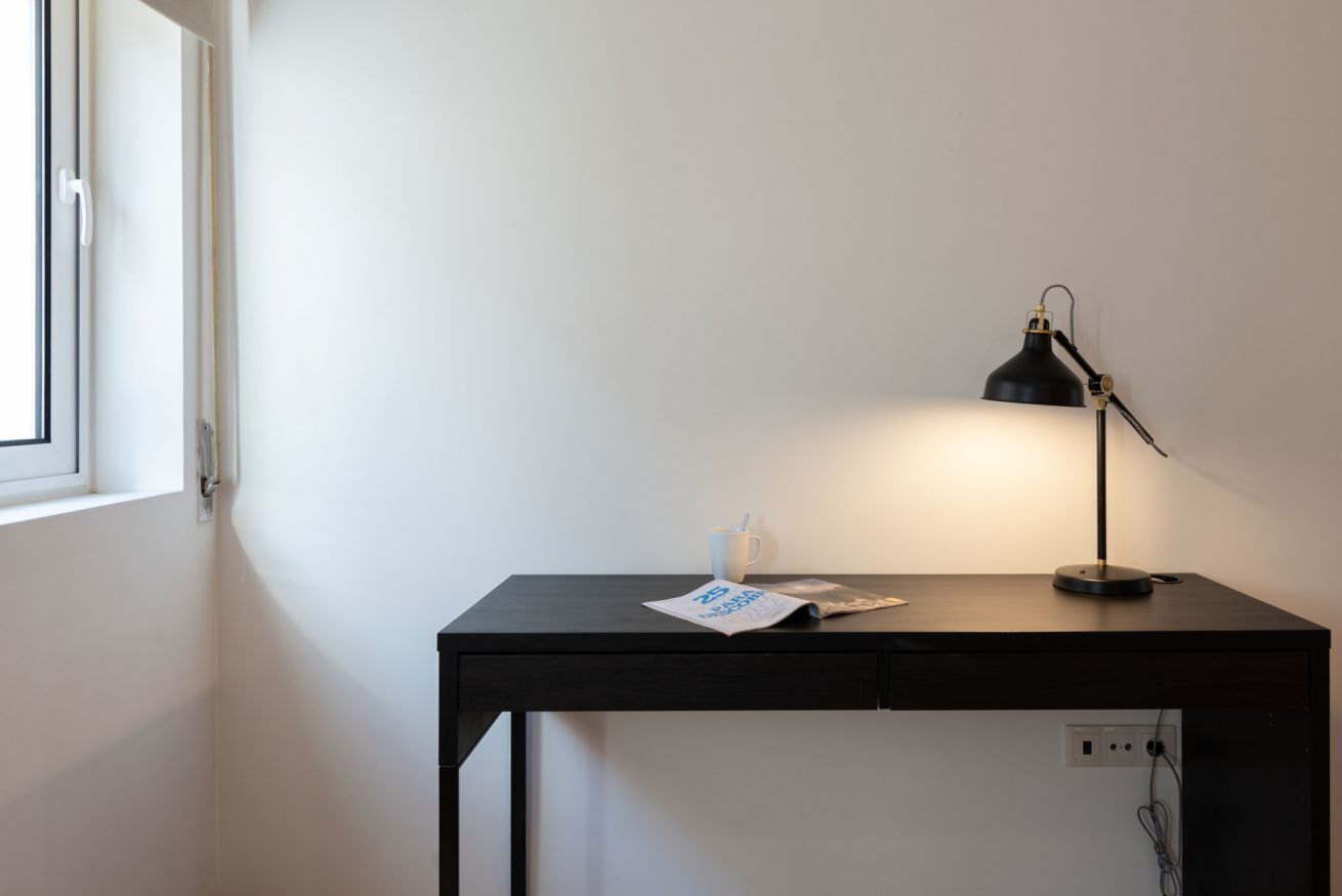 A small, dark wooden desk with a single black desk lamp, a white mug, and a newspaper.