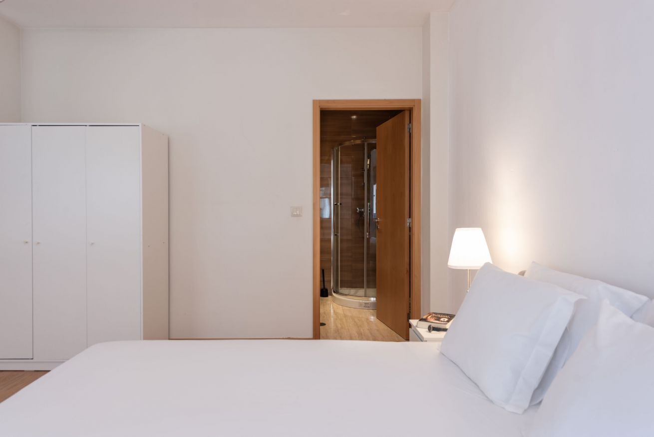 Ein Hotelzimmer mit Bett, Nachttisch, Lampe und einer Holztür zu einem Duschbereich.