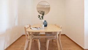 Et rundt træbord med fire stole, en vase med en plante, og et spejl på væggen.