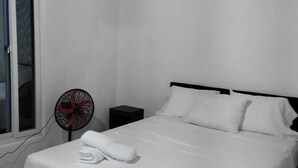 Une chambre à coucher avec un lit, un ventilateur, une table de chevet et une fenêtre.