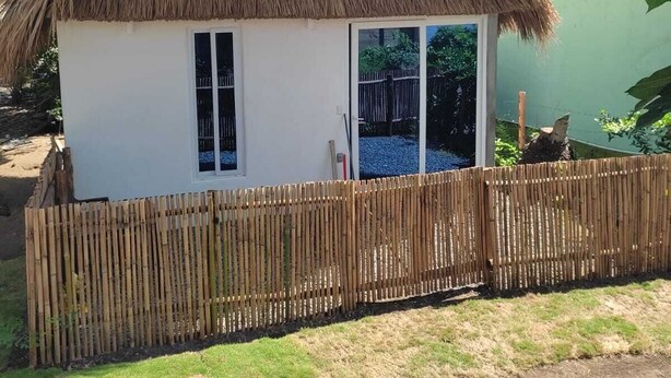 Une petite maison avec un toit de chaume et une clôture en bambou.