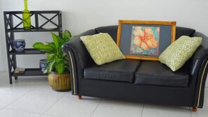 A black leather sofa with patterned cushions, a framed floral artwork, a potted plant, and a black metal shelf with decorative items.