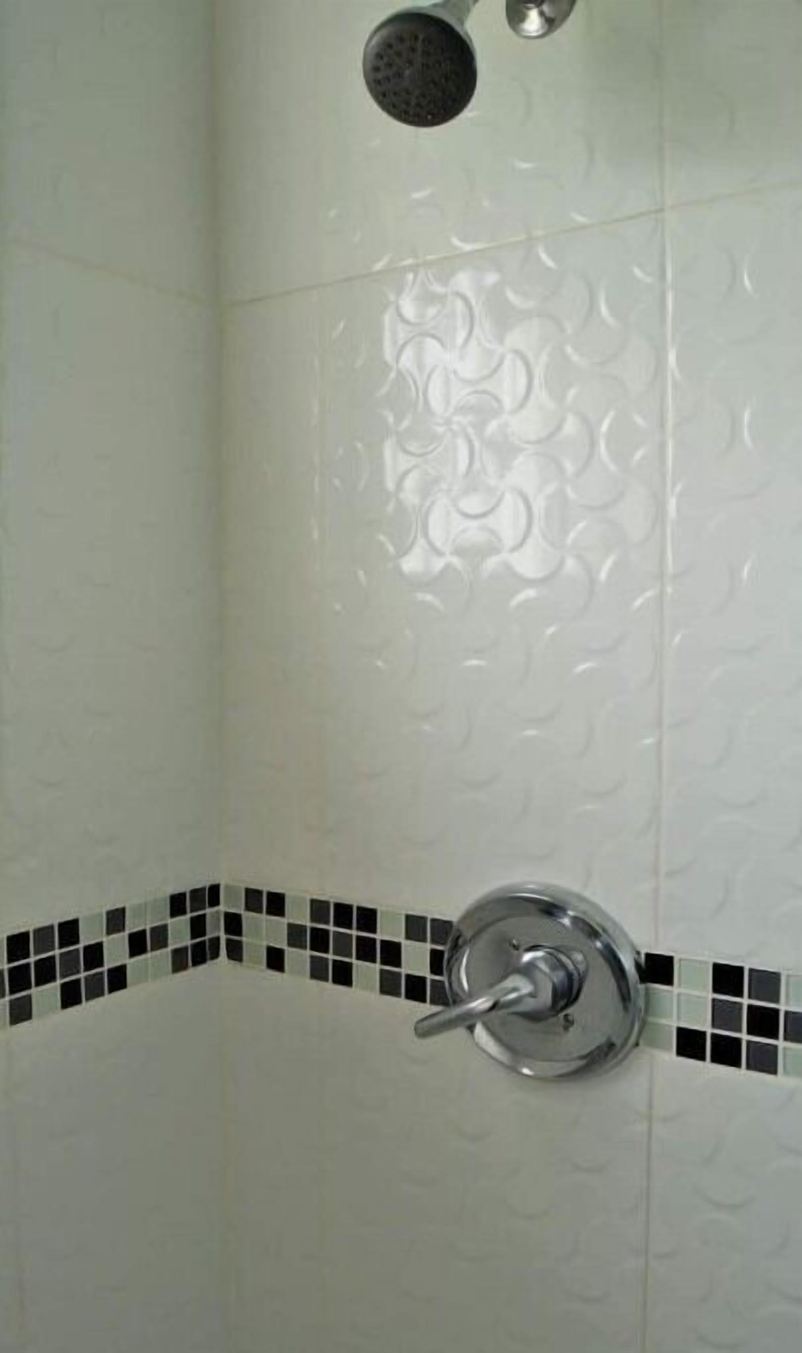 A shower with a chrome faucet and a textured wall.