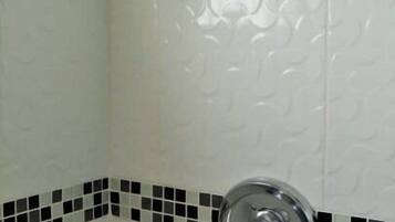 A shower with a chrome faucet and a textured wall.