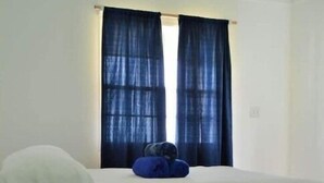 A room with a bed, a window with blue curtains, and a potted plant.