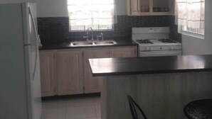 A kitchen with a refrigerator, sink, cabinets, and a stove.