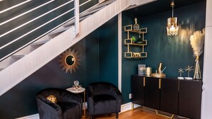 A staircase leading to a dark teal wall with a sunburst mirror, two black velvet chairs, a small round table, and a black console with gold accents. - Spacious! Game Room, near Restaurants, Bars, Shops, DT BFLO & Niagara Falls! (Buffalo)