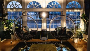 A room with two hanging chairs, a central table, and large windows with arched tops. - Spacious! Game Room, near Restaurants, Bars, Shops, DT BFLO & Niagara Falls! (Buffalo)