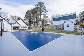 Ein Basketballplatz im Freien mit blauer Spielfläche, umgeben von einer Steinmauer und einem kleinen Schuppen.