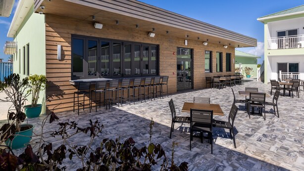 An outdoor seating area with tables and chairs, a wooden facade, and potted plants.