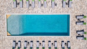 An aerial view of a rectangular swimming pool surrounded by rows of sun loungers with green towels.