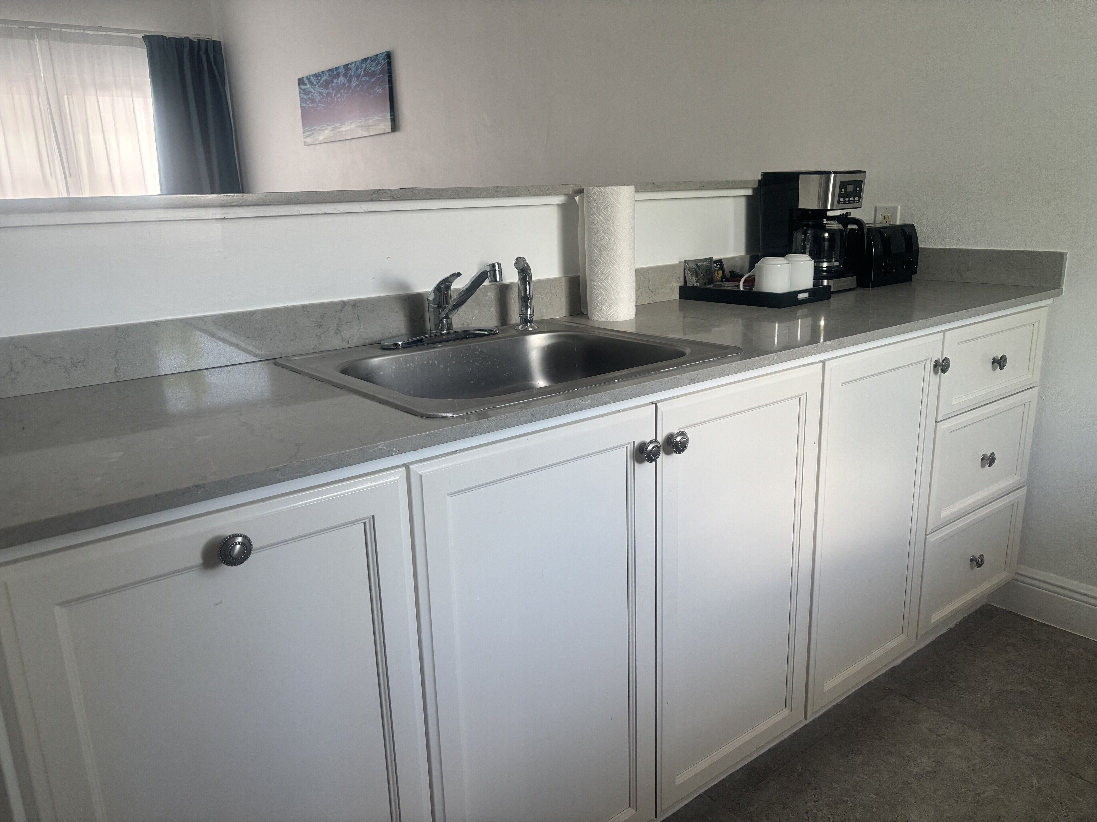 A kitchen with white cabinets, a stainless steel sink, and a coffee maker.
