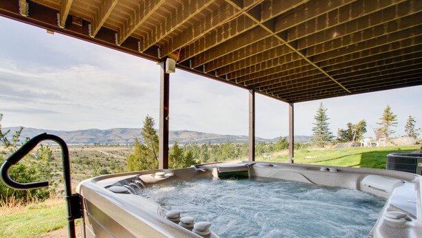 Een hottub onder een houten pergola, met een panoramisch uitzicht op de bergen.