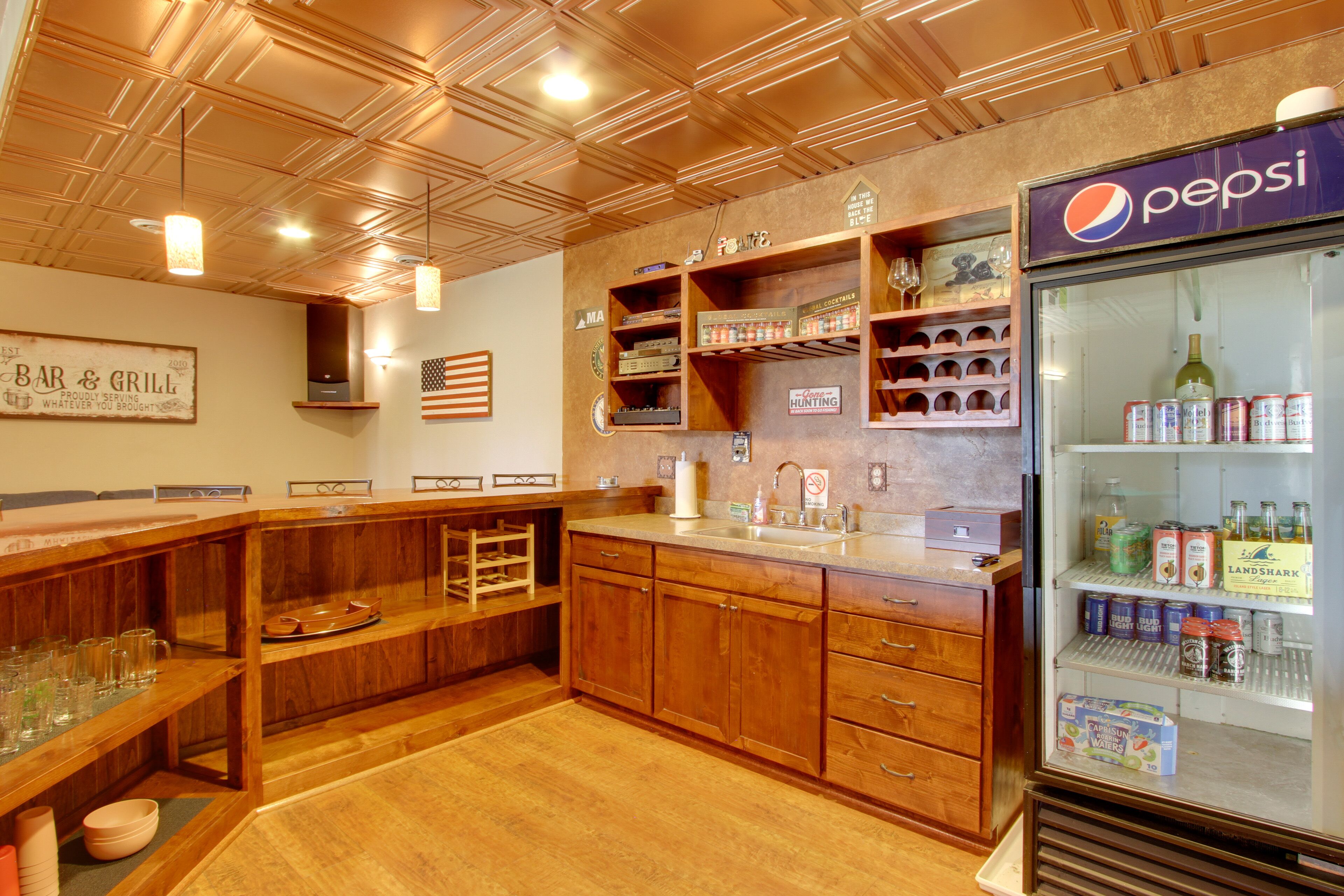 Una zona de bar con armarios de madera, estantes con botellas y un refrigerador de Pepsi.