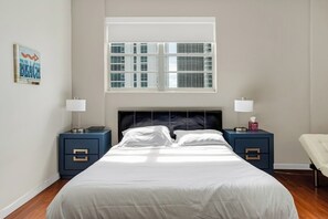 Une chambre à coucher comprenant un lit, deux tables de chevet, une fenêtre et une œuvre d’art accrochée au mur.