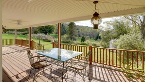 Une terrasse extérieure couverte, dotée d’une table en verre et de chaises en métal, qui offre une vue sur un jardin luxuriant et des arbres.