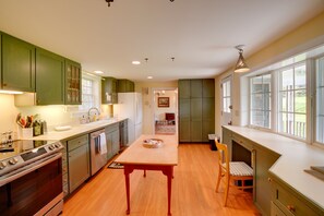 Una cocina con armarios verdes, una mesa de madera y un ventanal con vistas a un jardín.