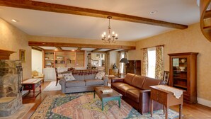 Un salon spacieux avec un grand canapé, une table basse et un tapis à motifs. On y trouve une cheminée, un meuble en bois et un lustre.