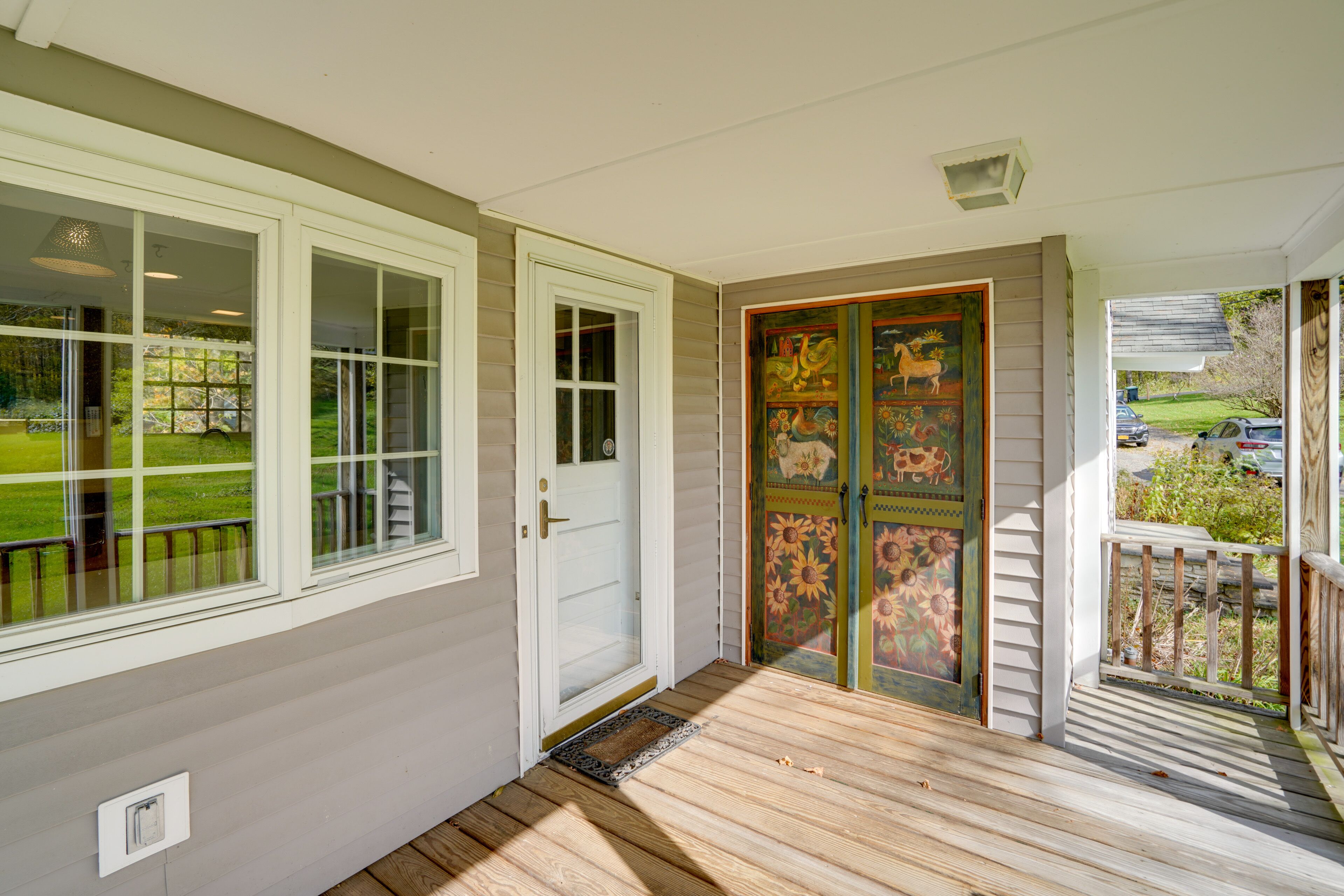 Un portico coperto con pavimento in legno, una porta bianca e una porta colorata con decorazioni floreali.