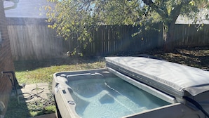 Een hottub met een gedeeltelijk open deksel, omringd door een houten hek en bomen.
