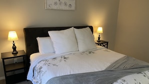 Een opgemaakt bed met een bloemenbedekking, twee bedlampjes en een kunstwerk aan de muur erboven.